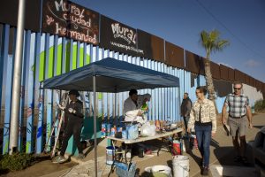 Turistas observan a los voluntarios que ayudan en la elaboración de murales en la cerca que marca el límite en la frontera entre EE.UU. y México hoy, jueves 1 de diciembre de 2016, durante el primer día de la realización de este proyecto en Tijuana (México). Un grupo de artistas inició hoy un proyecto sin precedentes bajo el cual cientos de voluntarios de distintas partes del mundo se unirán para ponerle color a más de dos mil metros lineales del muro fronterizo entre México y Estados Unidos. EFE